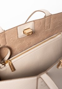 Borsa a mano in pelle beige con interni in pelle scamosciata color marrone chiaro, dotata di una chiusura e una cerniera dorate. Visibile una tasca con cerniera interna, con accessori in metallo.