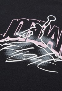 Il tessuto nero presenta un design grafico con la parola "JORDAN" in rosa, sovrapposta a una silhouette di un giocatore di basket in grigio e bianco.