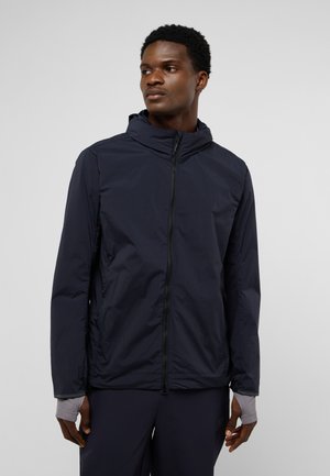 Veste légère bleu marine avec capuche, zipper frontal intégral, poches latérales et poignets élastiques. Texture lisse et design minimal.