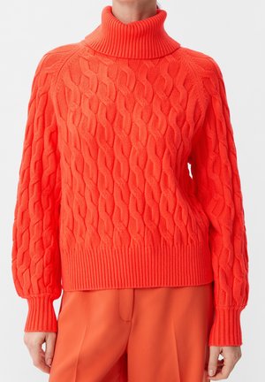 Femme portant un pull à col roulé en tricot torsadé orange vif avec des poignets côtelés et un pantalon orange assorti.