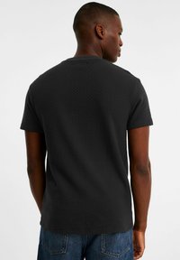 Sort tekstureret T-shirt med korte ærmer og runde halsudskæring, med et diskret ternet mønster og sømløs rygdesign.