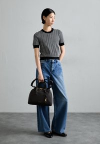 Zwart-wit gebreide top met patroon, brede blauwe denim broek en een gestructureerde zwarte handtas met gouden accenten en dubbele handvaten.