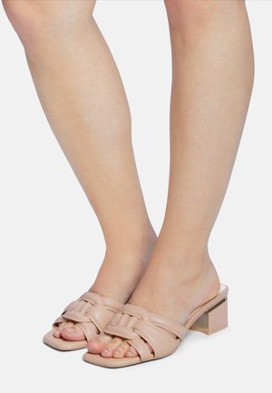 Mules à talons hauts en cuir tan avec un design noué sur les orteils, une forme de pied carrée et un talon en bloc géométrique.