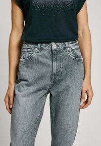 Vaqueros de mezclilla gris de cintura alta con un corte relajado, que cuentan con bolsillos frontales y un cierre clásico de botón. Tejido de algodón con un acabado deslavado.