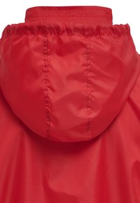 Giacca impermeabile rossa con cappuccio regolabile, texture liscia e design elegante e moderno. Leggera, adatta a diverse condizioni atmosferiche.
