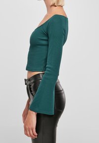 Tyrkysový, těsně padnoucí dlouhý rukáv top s širokým výstřihem a rozšířenými rukávy, v kombinaci s kalhotami z černé ekokůže s vysokým pasem.