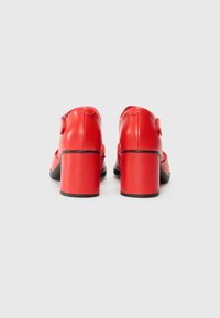 Red leather high-heeled shoes with a squared block heel, smooth texture, and black accents. Zipper detail at the back.