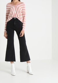 Roze en witte gestreepte gebreide trui met een wijde halslijn, gecombineerd met hoge zwarte flare jeans en witte enkellaarsjes.