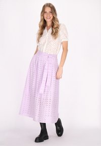 Blusa bianca in pizzo broderie anglaise con maniche corte abbinata a una gonna midi in lilac con occhielli e cintura da annodare, indossata con stivaletti neri alla caviglia.