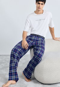 Námornícke kárované pyžamové nohavice s červenými a bielymi akcentmi, ktoré majú elastický pás s logom TOMMY HILFIGER, skombinované s bielym tričkom.
