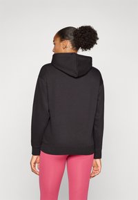 Svart bomullslue med en tilpasset design, stor hette og ribbede mansjetter, kombinert med rosa leggings. Slank tekstur, minimalistisk stil.
