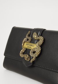 Black leather clutch with gold snake-shaped clasp and "Just Cavalli Milano" engraved on the metal plate.