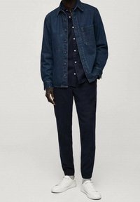 Tmavě modrá džínová bunda s kapsou na hrudi, kombinovaná s tmavou košilí s knoflíky a námořnickými kalhotami, doplněná bílými teniskami.