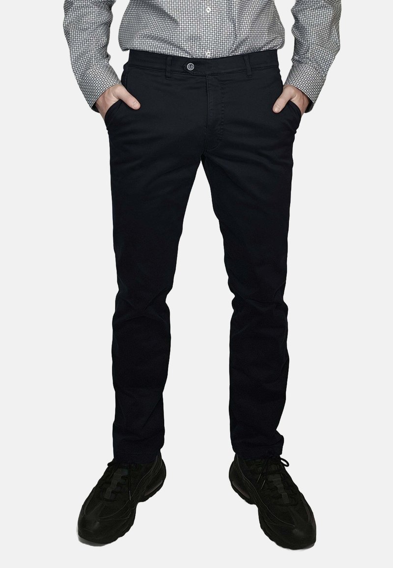 Pantaloni neri slim fit in cotone con una texture liscia. Tasche frontali, chiusura con bottoni, abbinati a scarpe sportive nere.