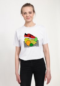 Bílá tričko s grafikou červených tenisek a barevného ovoce. Design zahrnuje žluté banány, zelené a oranžové tvary a černé akcenty.