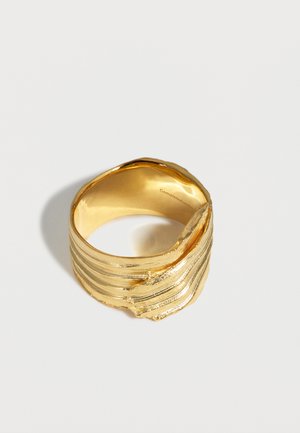 Anillo ancho de oro con estrías texturizadas y un diseño irregular y plegado en un lado, mostrado sobre un fondo blanco.