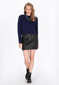 Maglione navy con dettagli sulle spalle, abbinato a una mini gonna in pelle nera con zip frontali. Stivali alla caviglia neri con lacci completano il look.