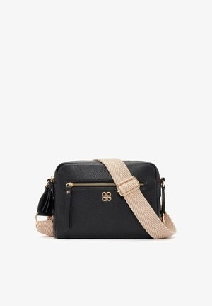 Sac bandoulière en cuir noir avec poche avant zippée, fermeture éclair dorée et logo, et large bandoulière beige réglable avec motif chevron.