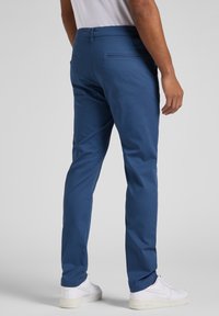 Modré bavlněné chino kalhoty s úzkým střihem, hladkou texturou, zadními kapsami a prošitou pásovkou, doplněné bílými teniskami.