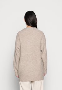 Suéter beige de punto extragrande con dobladillo acanalado y mangas largas, que presenta una textura suave y un diseño sencillo y discreto.