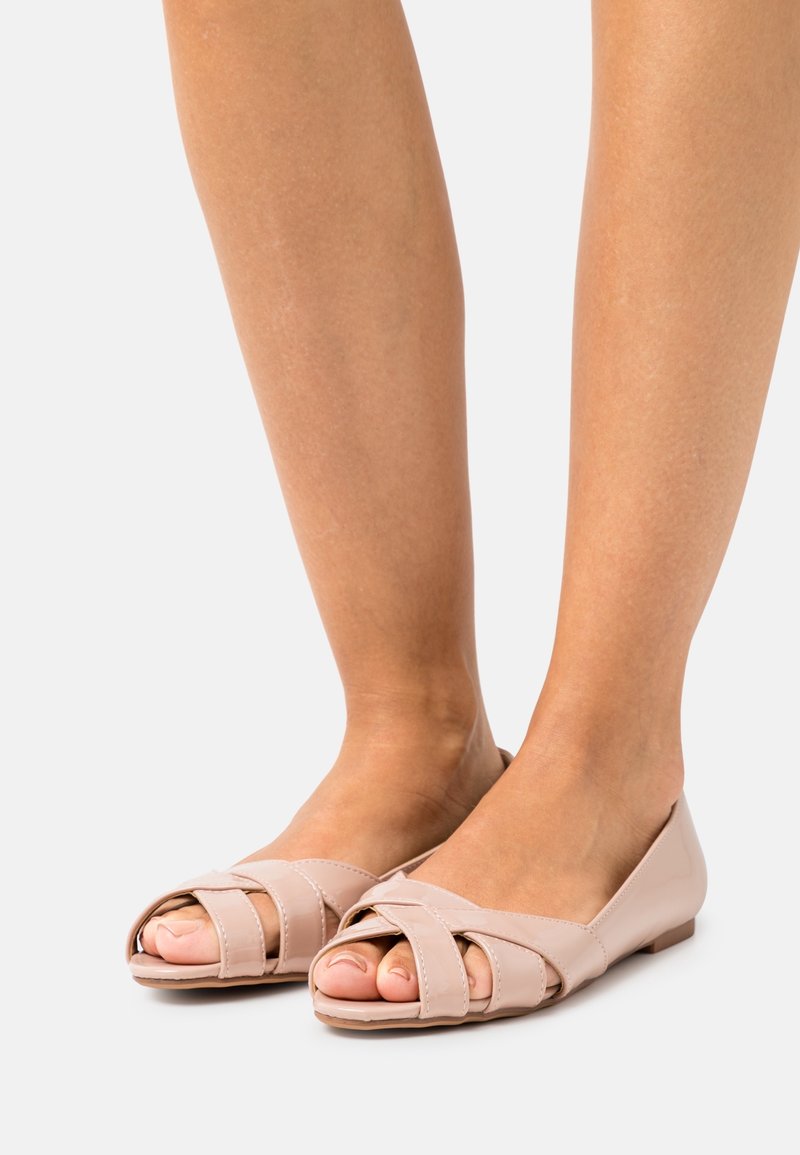 Flats beiges à bout ouvert avec un design à bride croisée, en cuir lisse, dotées d'une semelle basse et plate et d'une construction minimaliste.