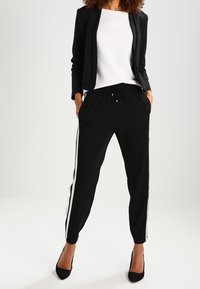 Černý dobře padnoucí blazer, bílý textured top a černé joggingové kalhoty s bílými bočními pruhy. Černé podpatky dokončují outfit.