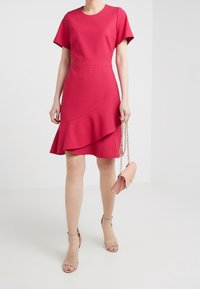 Różowa sukienka z krótkimi rękawami, dopasowaną górą i falbaniastym dołem. Akcesorium to mała torebka w odcieniu blush róż z łańcuszkowym paskiem.