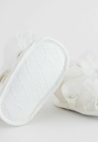 White baby sandals made of soft fabric with tulle accents, open design, textured rubber sole, and a secure strap for comfort.