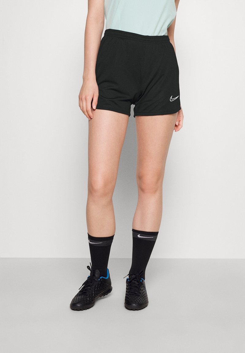 Shorts atléticos negros con una cinturilla elástica, con un logo de Nike en blanco. Combinados con calcetines negros y zapatillas negras texturizadas.