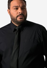 Zwarte dress shirt met een puntkraag, lange mouwen en een borstzak. Heeft een zachte textuur en een zwarte stropdas.