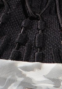 Schwarzes Strick-Obermaterial mit strukturiertem Oberfläche, ausgestattet mit elastischen Schnürsenkeln und einer weißen Camouflage-mustered Sohle. Enthält subtile Hardware-Akzente.