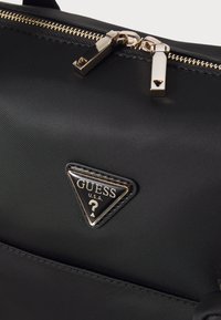 Sort nylon håndtaske med guldtonet hardware, der har et markant trekantet logo og lynlås lukninger. Glat tekstur med minimale accenter.