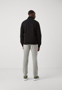 Sudadera negra con cuello alto, pantalones de chándal grises y zapatillas verdes. El conjunto tiene un corte relajado y está hecho de materiales suaves.