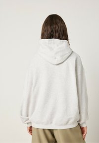 Sudadera de gran tamaño en gris claro, hecha de una tela suave, con una capucha amplia, hombros caídos y puños y dobladillo acanalados.