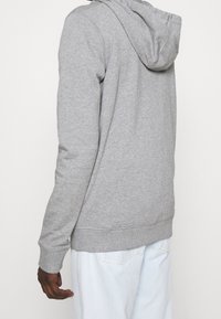 Sudadera con capucha gris de tejido suave, con mangas largas, un bolsillo canguro en la parte frontal y puños y dobladillo acanalados. Diseño minimalist.