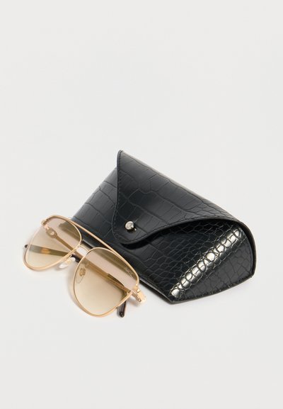 Γυαλιά ηλίου aviator με χρυσό πλαίσιο και καφετί σκουρόχρωμους φακούς δίπλα σε μαύρη υφή δερμάτινη θήκη για γυαλιά με κούμπωμα κουμπιού.