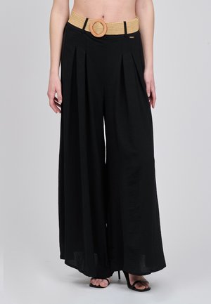 Schwarze, weit geschnittene Hose mit Falten, ausgestattet mit einem dicken, gewebten beigefarbenen Gürtel mit runder Schnalle. Glatter Stoff mit leicht strukturierter Optik.