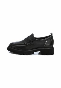 Zapato negro de cuero tipo slip-on con punta redondeada, parte superior texturizada, correa decorativa con hebilla y suela de goma gruesa con un patrón de relieve.