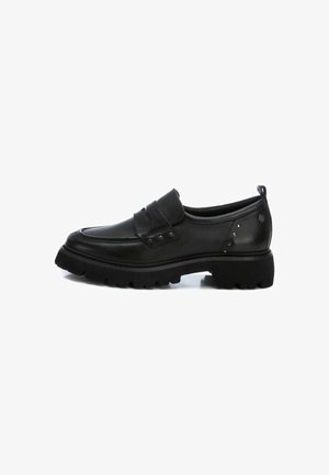 Zapato negro de cuero tipo slip-on con punta redondeada, parte superior texturizada, correa decorativa con hebilla y suela de goma gruesa con un patrón de relieve.