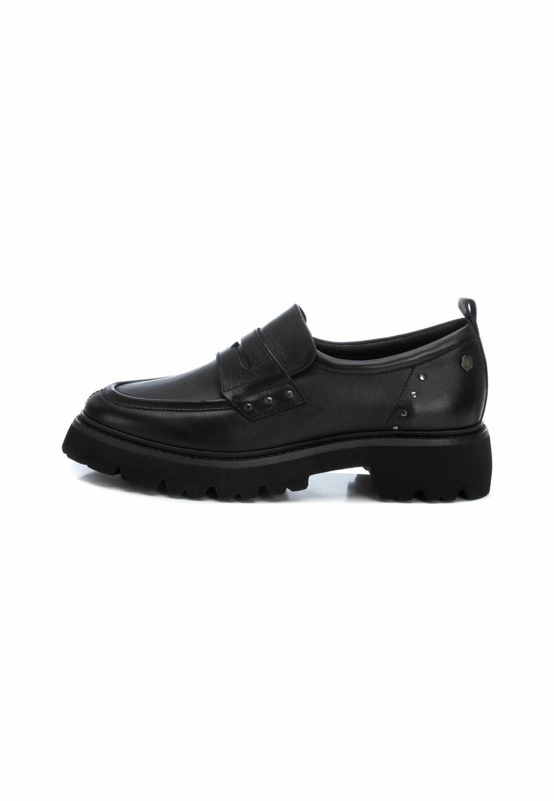Zapato negro de cuero tipo slip-on con punta redondeada, parte superior texturizada, correa decorativa con hebilla y suela de goma gruesa con un patrón de relieve.
