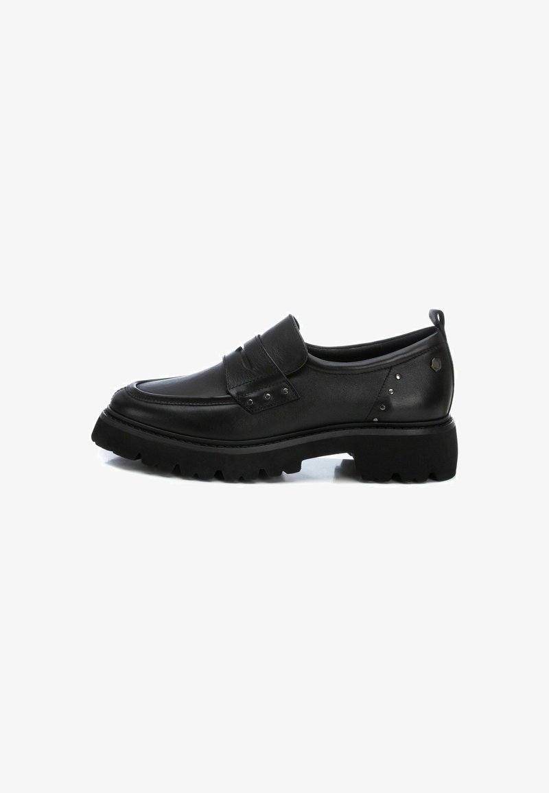 Zapato negro de cuero tipo slip-on con punta redondeada, parte superior texturizada, correa decorativa con hebilla y suela de goma gruesa con un patrón de relieve.