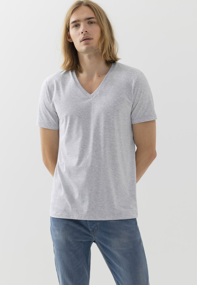 T-shirt grigia a V in cotone morbido, maniche corte e taglio rilassato. Indossata con jeans blu, caratterizzati da un design semplice e una texture liscia.