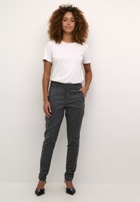 Pantalons gris ajustés avec une coupe slim et des poches latérales, associés à un T-shirt blanc. Les chaussures sont noires avec des pointes et des accents décoratifs.