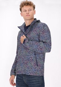 Jachetă marină cu un model geometric multicolor, cu un guler înalt, buzunare cu fermoar și un material ușor, texturat.