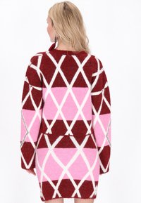 Röd och rosa tröja med diamantmönster, som har långa ärmar, en texturerad yta och vita detaljer på ett mjukt tyg.