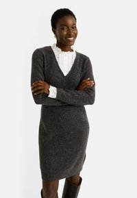 Vestido de punto gris carbón con escote en V, mangas largas y silueta ajustada. Superpuesto con una camisa blanca de cuello con bordado en ojal.