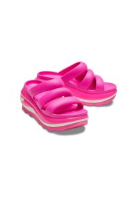 Różowe gumowe klapki z czterema skrzyżowanymi paskami i grubą podeszwą z białymi akcentami. Projekt charakteryzuje się fakturowaną powierzchnią dla lepszego chwytu.