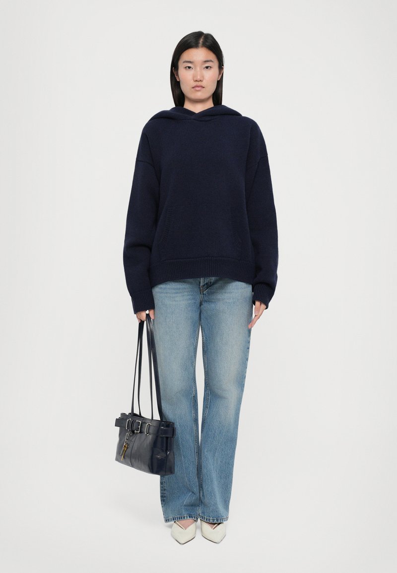 Navy oversized hoodie with a front pocket, paired with light blue flared jeans and a small black handbag featuring a belt detail and keychain.