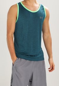 Teal träningslinne med ljusgröna accenter, rund halsringning och en ventilerande textur. Bärs med grå shorts med ett mönstrat sidofält.