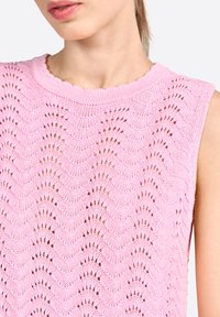 Débardeur rose tricoté sans manches avec un motif en vagues, orné de détails ajourés et d'un col côtelé, mettant en avant un tissu texturé.